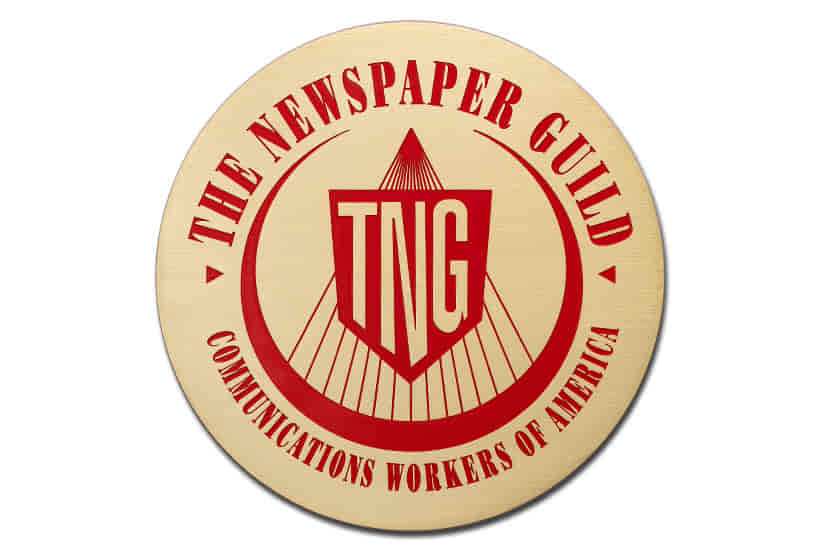 A round brass plaque with a brushed finish featuring "The Newspaper Guild" logo in red with bold text and color-filled details. 