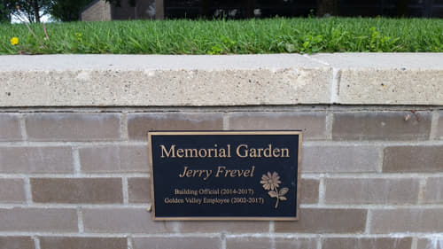 Bronze memorial plaque for Jerry Frevel on a brick wall, marking the Memorial Garden in his honor.